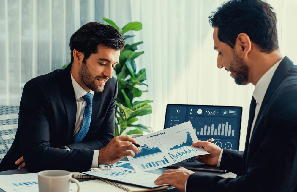 Two financial consultants discussing growth strategy using performance charts and analytics - business valuation