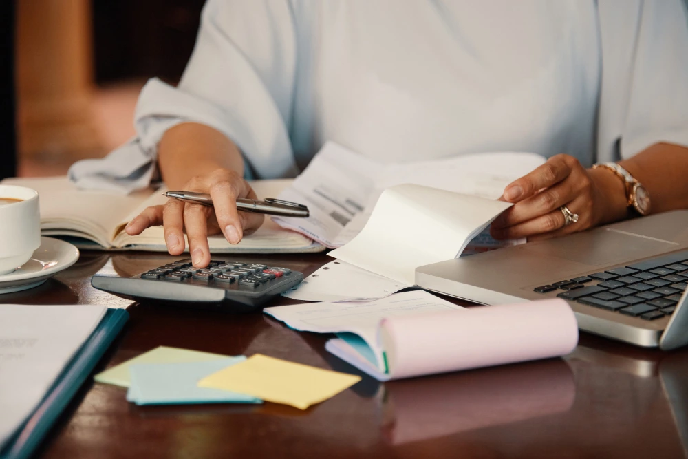 Person working with financial documents using a calculator and laptop at a desk - transfer pricing