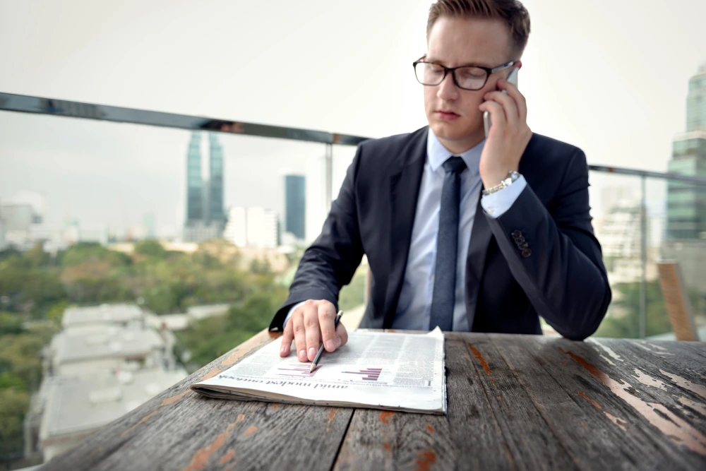 Professional man discussing business strategy on phone while reviewing stock market news outdoors - due diligence