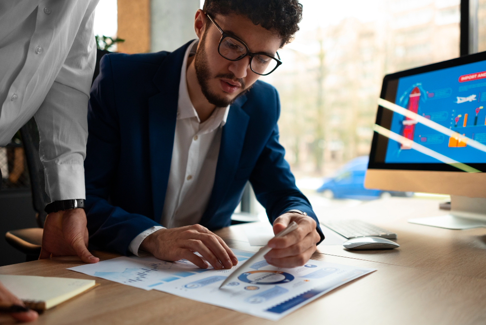 Professional reviewing financial charts and documents on a desk, collaborating with a colleague, illustrating efficient Due Diligence Workflows in a modern office setting.