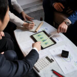 Business professionals reviewing financial charts and data on a tablet and documents during a meeting, highlighting challenges in Business Valuation and collaborative financial analysis.