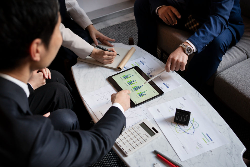 Business professionals reviewing financial charts and data on a tablet and documents during a meeting, highlighting challenges in Business Valuation and collaborative financial analysis.