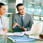 Business professionals in a meeting discussing financial reports and strategy over a laptop, representing effective Due Diligence Outsourcing and collaborative decision-making.