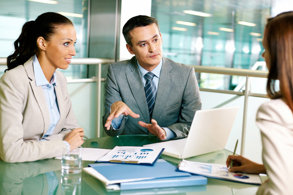 Business professionals in a meeting discussing financial reports and strategy over a laptop, representing effective Due Diligence Outsourcing and collaborative decision-making.